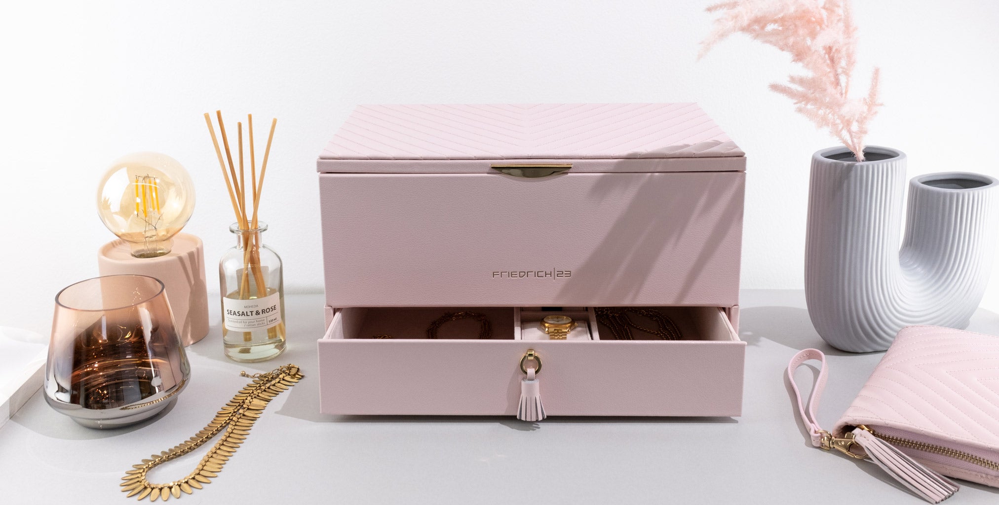 Rosa Leder Schmuckkoffer mit geöffneter Lade, passendem Etui und Schmuck, dekoriert mit Wohnaccessoires.