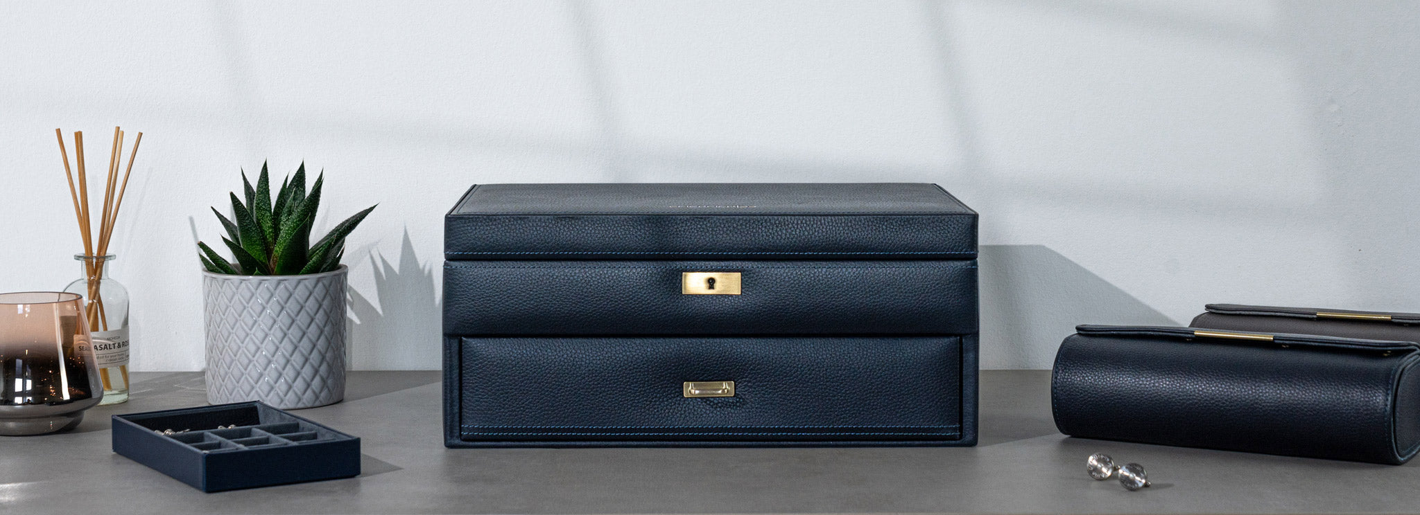 Dunkelblauer Leder Uhrenkoffer mit Manschettenfach und passender Uhrenrolle, edle Messingdetails.