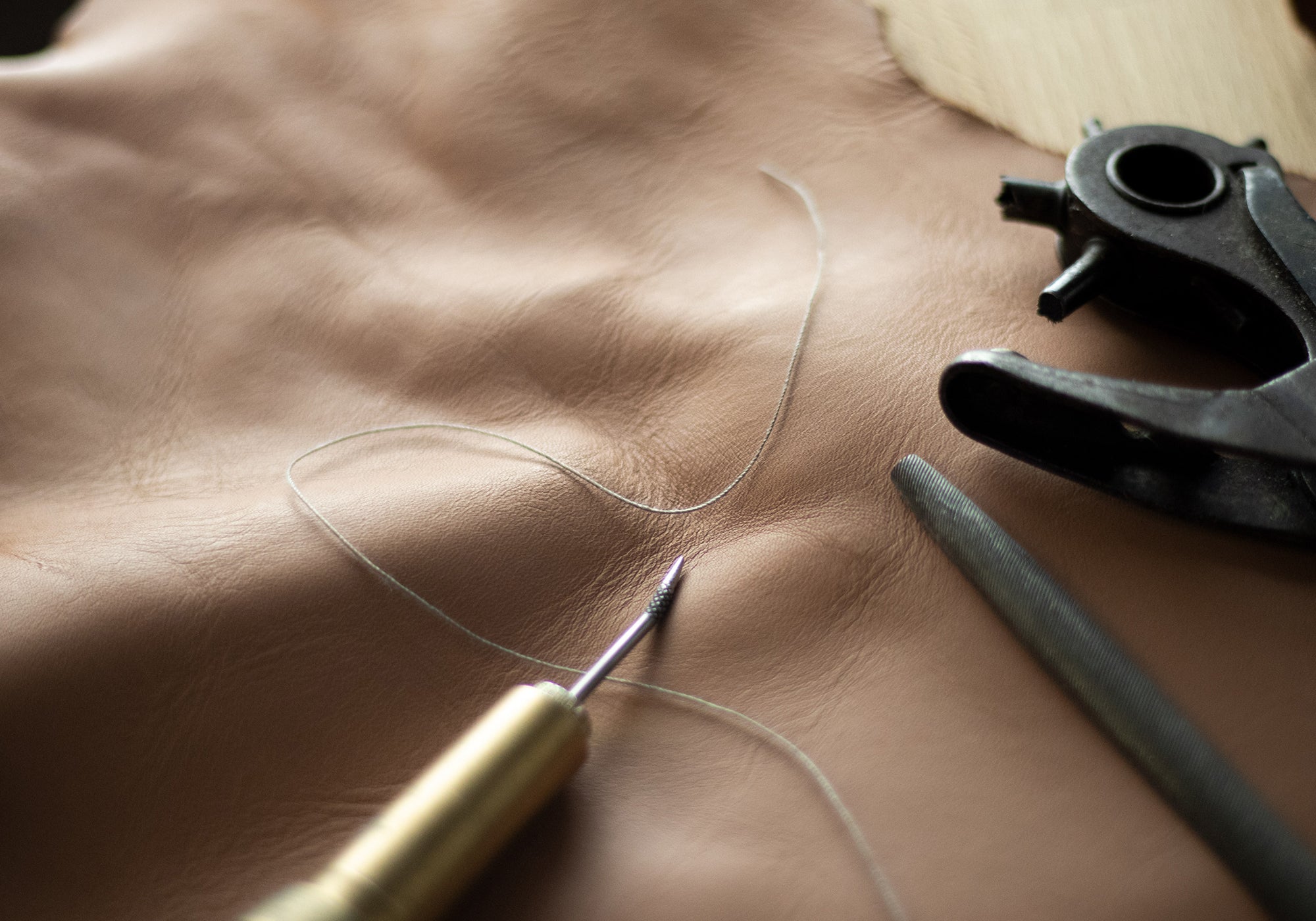 Hellbraunes Lederstück mit Werkzeugen – Zubehör zum Bearbeiten von Leder.