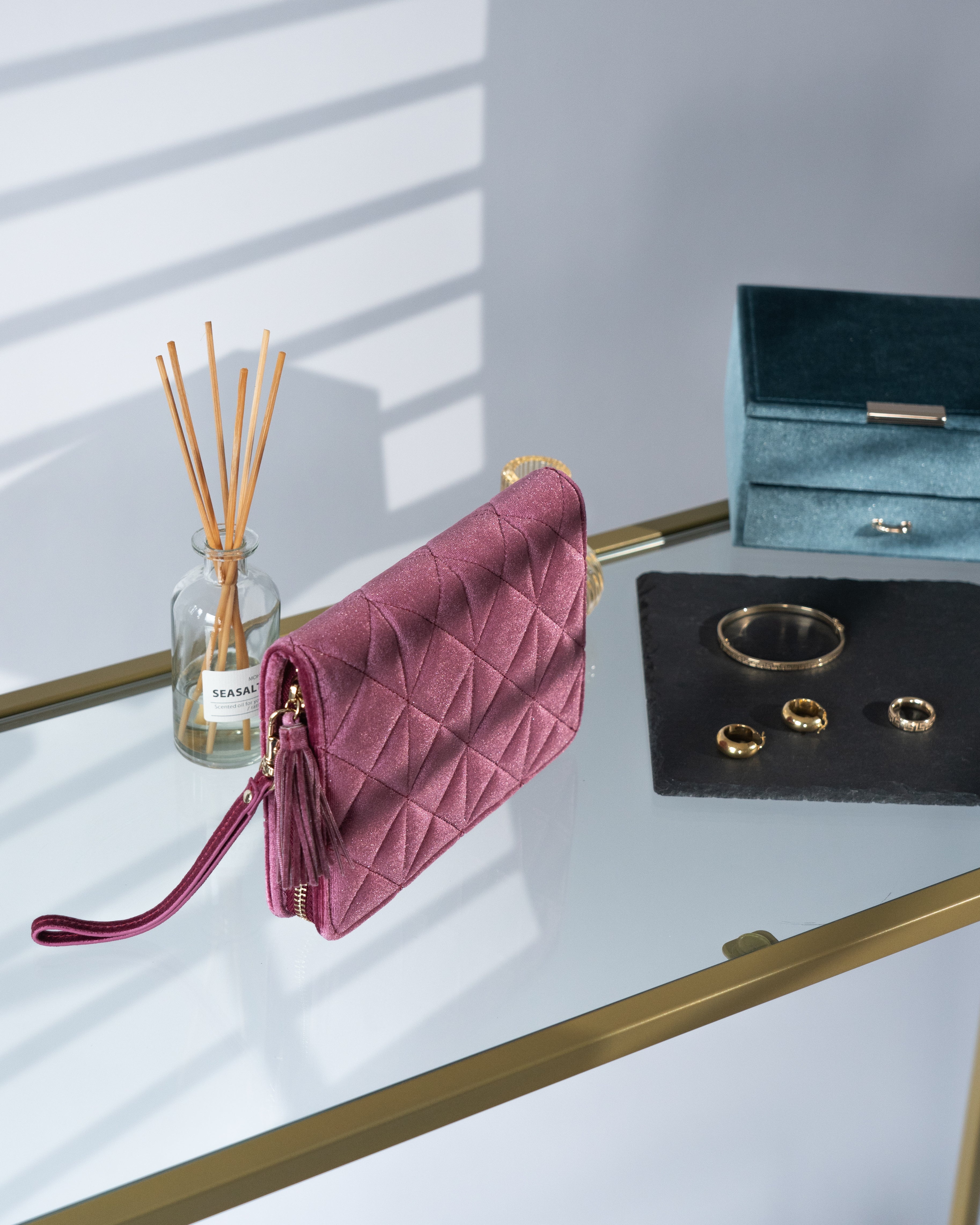 Schmucketui aus Samt in Fuchsia mit Steppmuster, Zierquaste und Handschlaufe auf Glastisch neben Schmuck