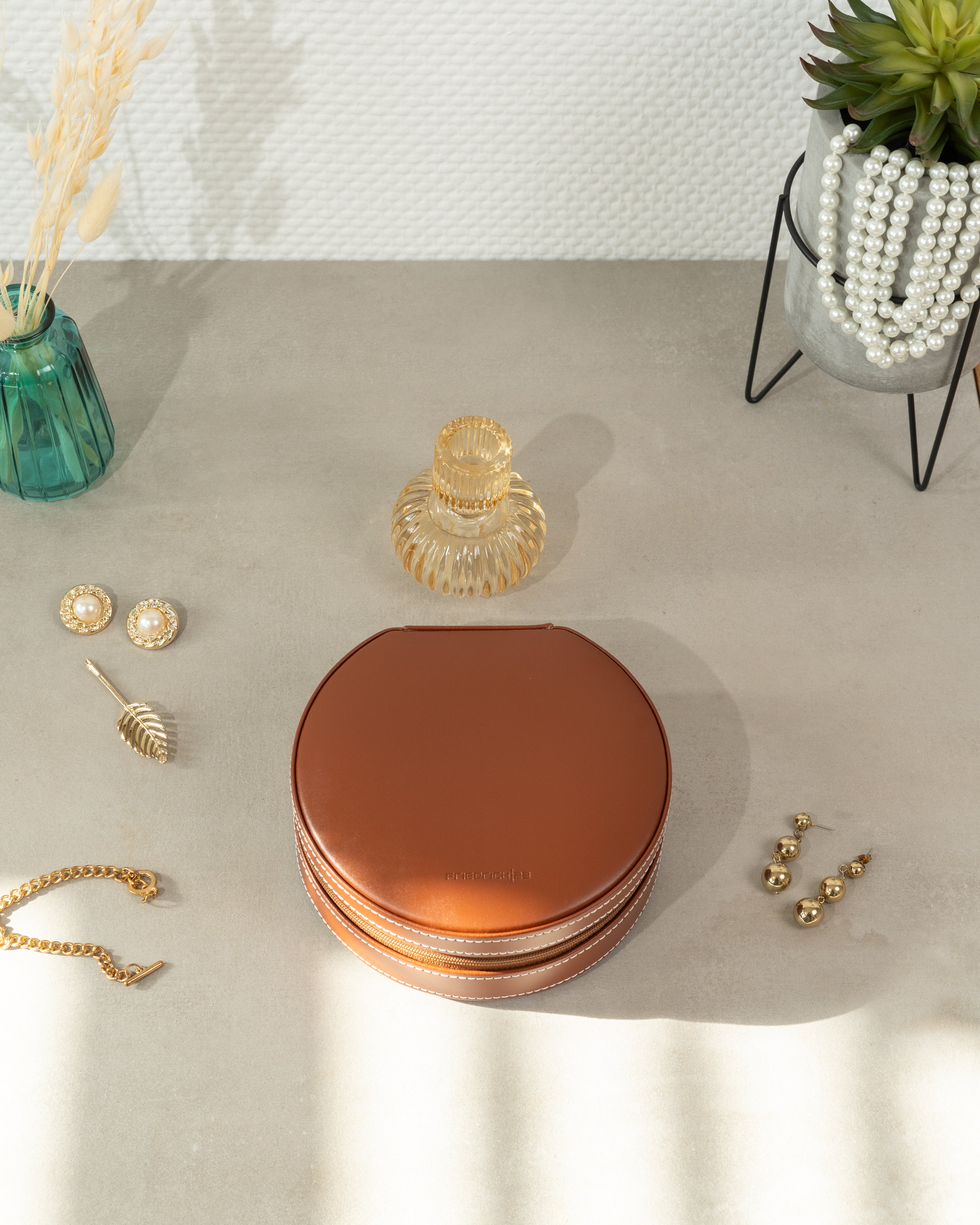 Braunes, rundes Schmucketui aus Leder mit weißen Ziernähten und Reißverschluss zwischen Accessoires und Schmuck.