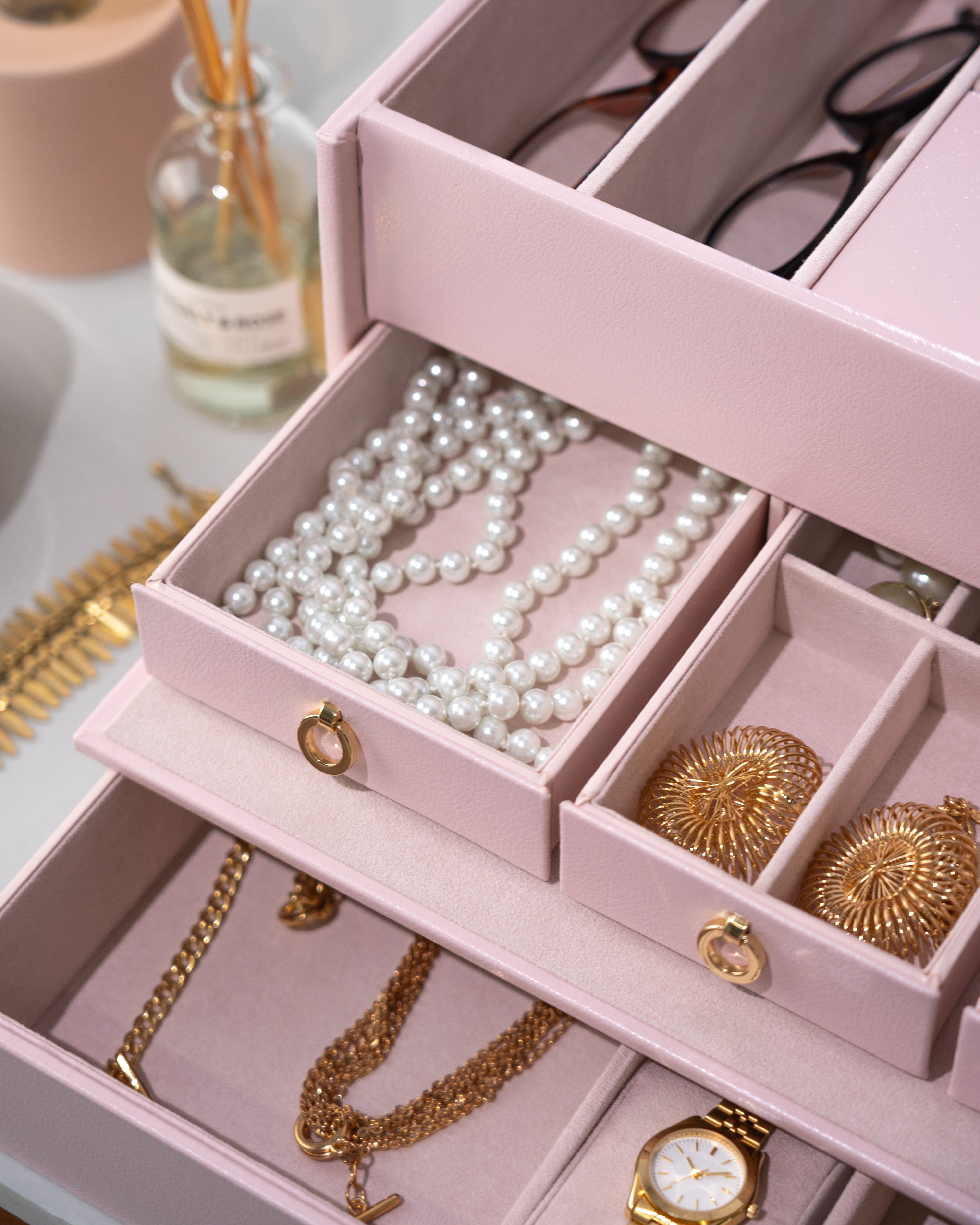 Detailaufnahme von geöffnetem rosa Schmuckkoffer aus Leder befüllt mit Schmuck, Uhren und Brillen.