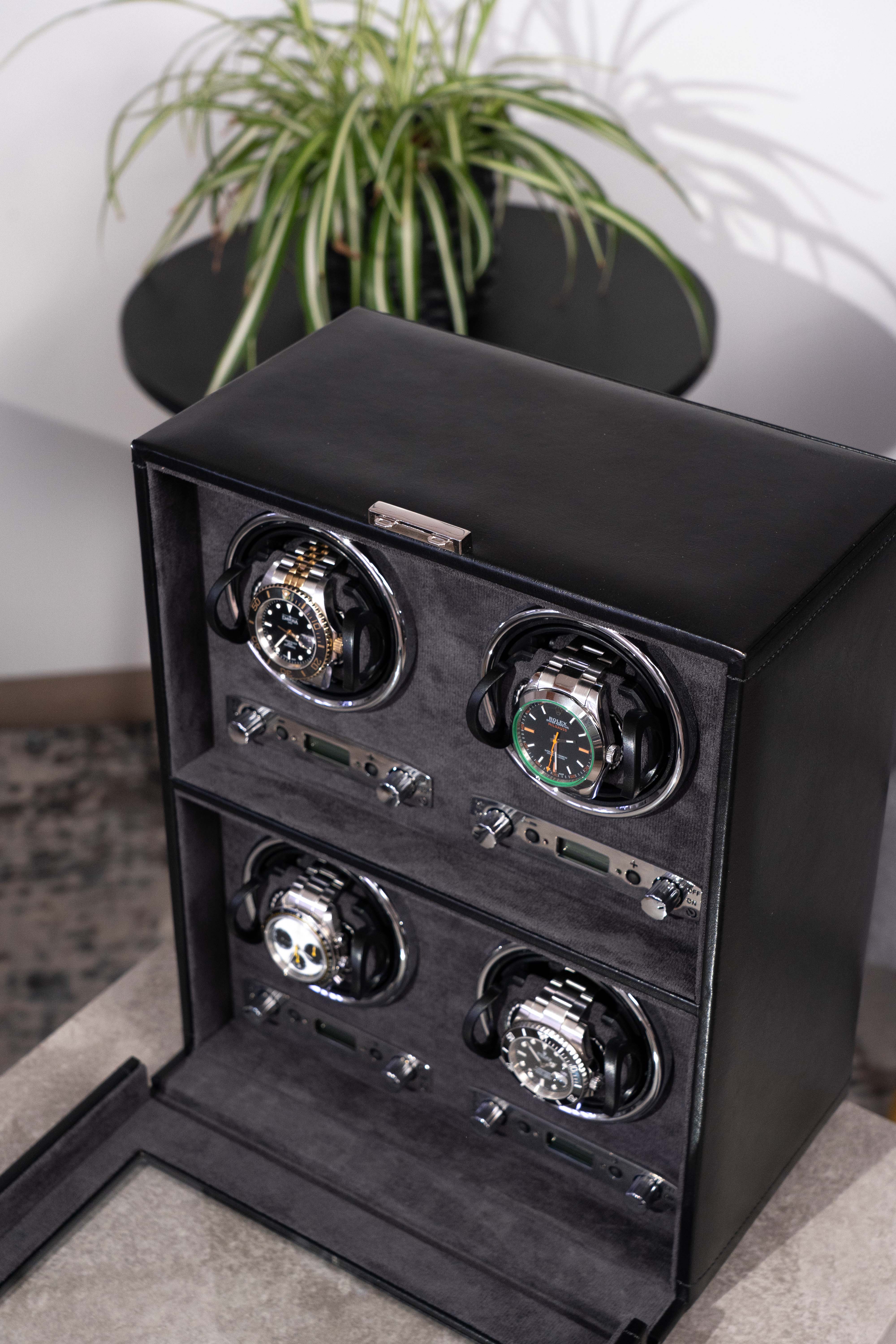 Detailansicht Uhrenbeweger aus schwarzem Leder mit Glasfenster für 4 Uhren, schräg auf Tisch stehend mit 4 Uhren bestückt.