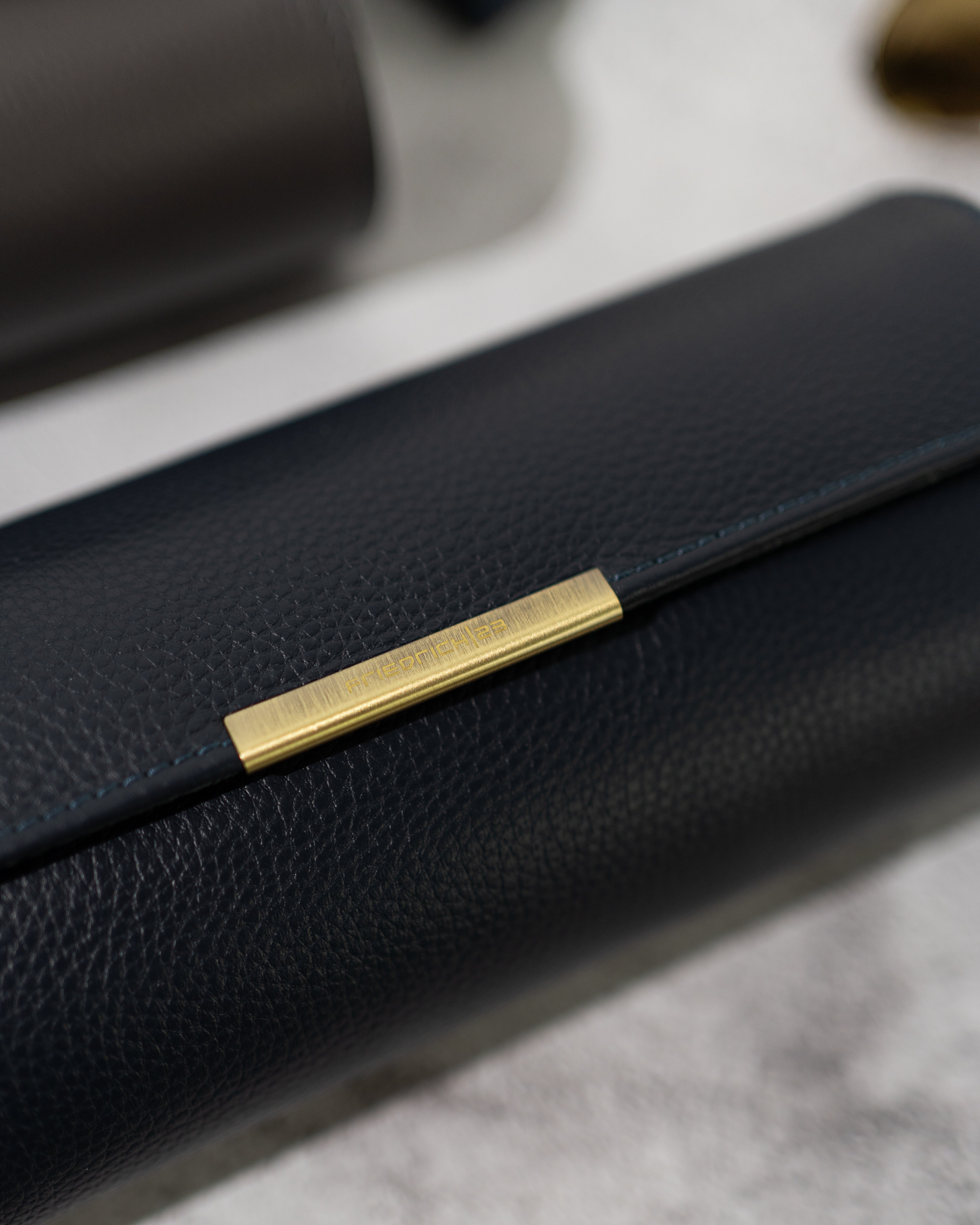 Detailaufnahme vom genarbtem Leder in dunkelblau, Lasche mit Metall Clip aus Messing mit Logo