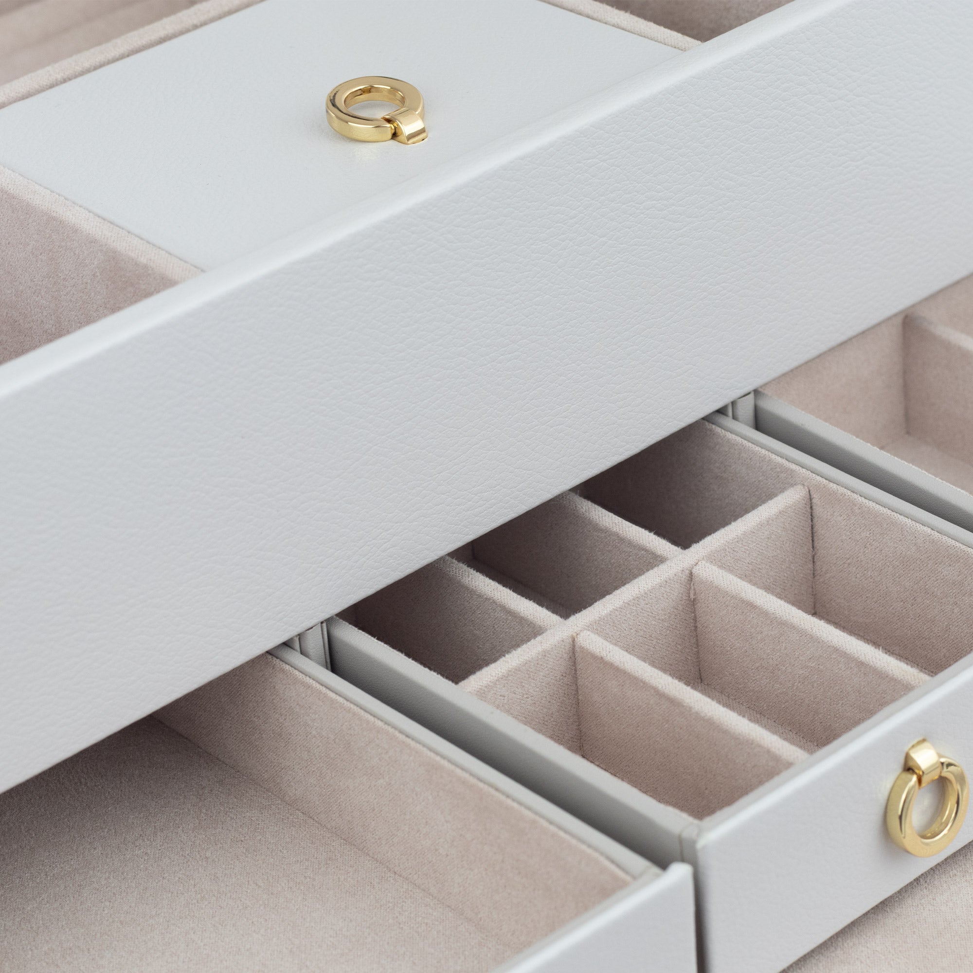 Detailaufnahme hellgrauer Schmuckkoffer aus Leder mit Laden und Fächern sowie Details in Goldoptik.