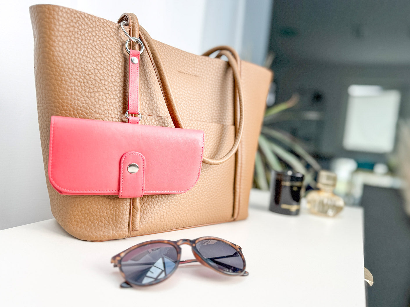 Nahaufnahme vom Brillenetui welches an einer Handtasche hängt und davor liegt eine Sonnenbrille