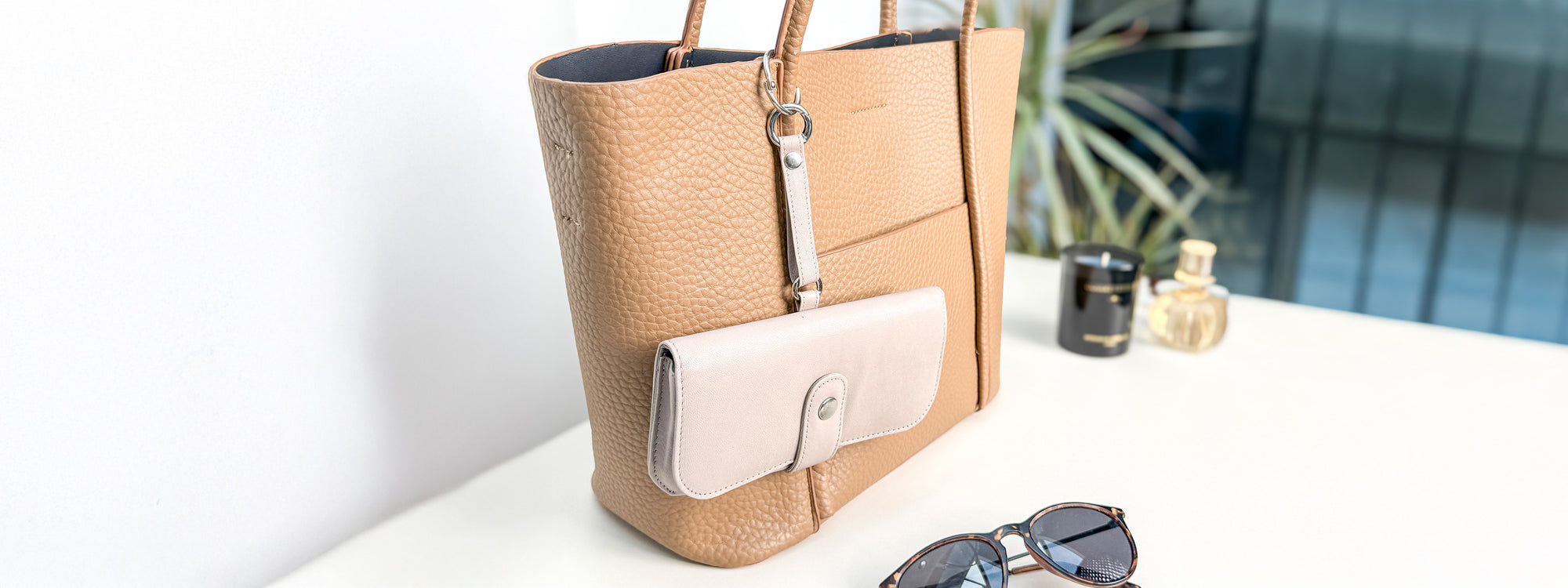 Handtasche auf einer Kommode mit einem am Hänkel befestigten Brillenetui für Sonnenbrillen oder Lesebrillen