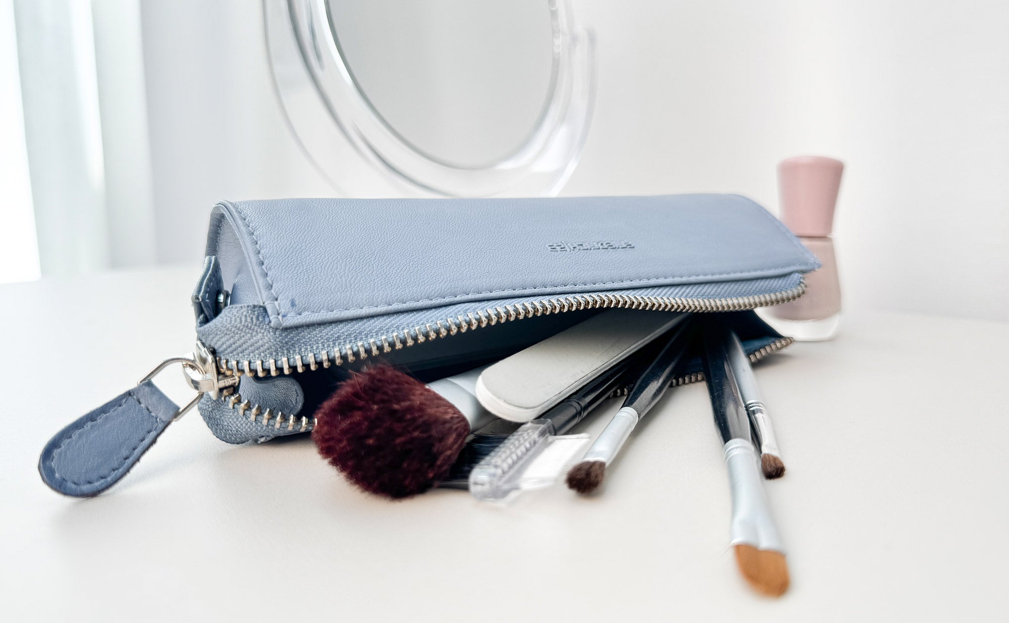 Beauty-Stifterolle aus Leder liegt geöffnet auf einer Kommode mit Spiegel und Beautyartikeln, der Reißverschluss ist geöffnet und mehrere Schminkpinsel sind sichtbar.